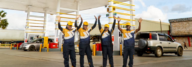  Four staff members dressed in company uniform with their arms raised and smiling, standing on the forecourt of an UNO Energies filling station.