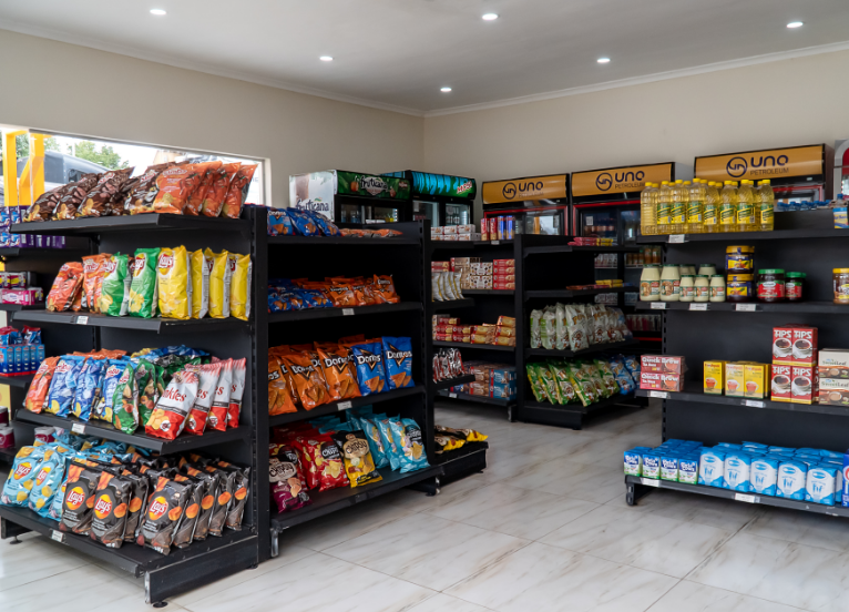 Inside view of a filling station convenience store showing three racks that contain potato crisp chips and various other snack and grocery items